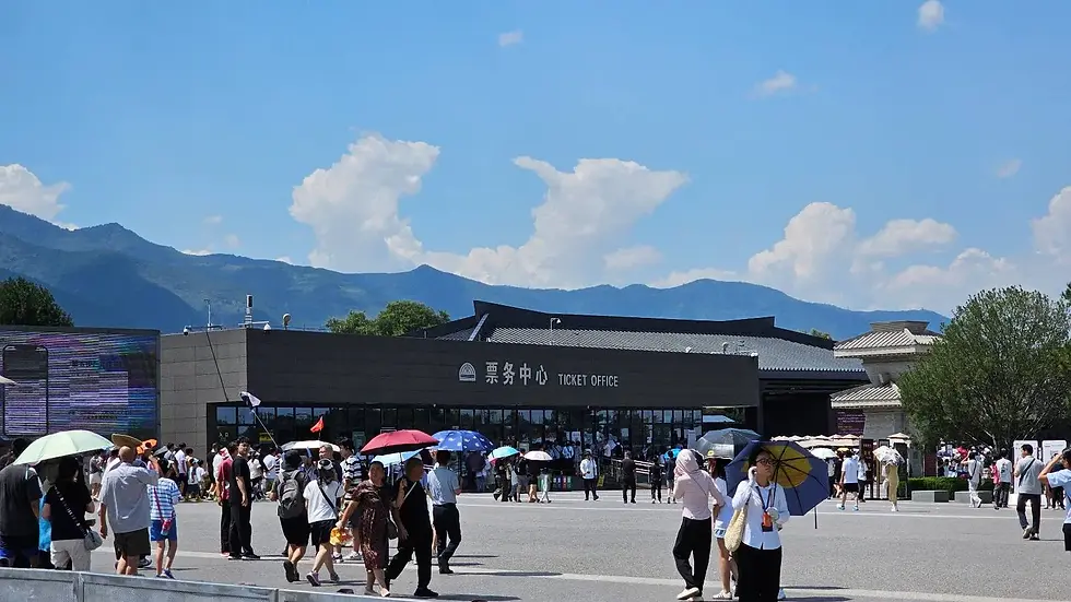 Crowd outside a ticket office under a clear blue sky with mountain backdrop. People hold colorful umbrellas, creating a lively, sunny scene.