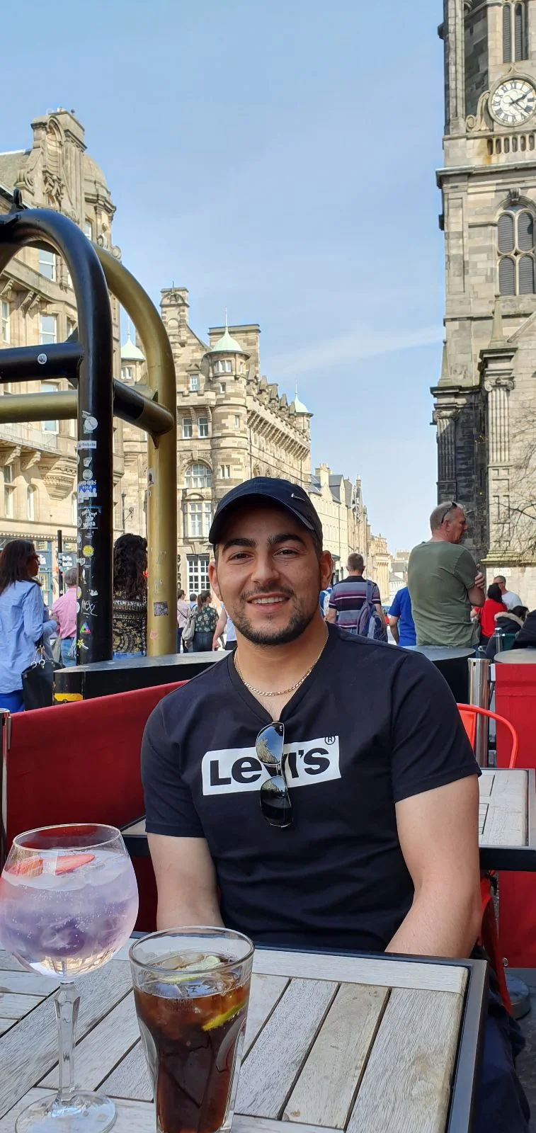Leon sitting at an outdoor café on the Royal Mile, with a drink on the table and Edinburgh’s historic streets behind.