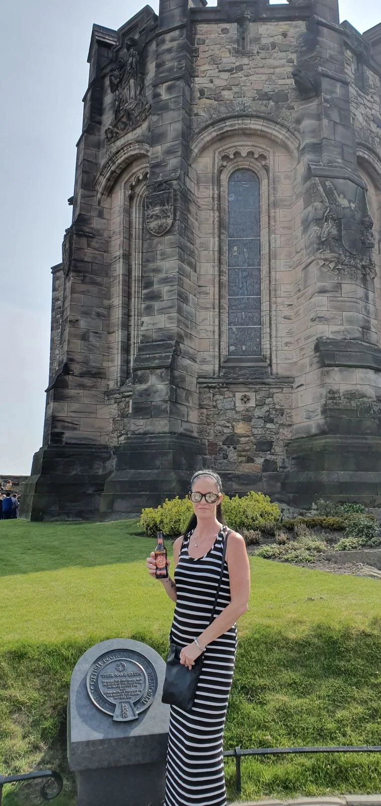 Woman holding a drink standing in front of the Scottish National War Memorial at Edinburgh Castle.