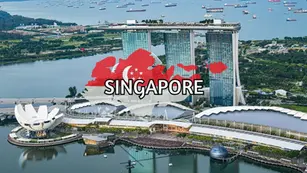 Aerial view of Marina Bay Sands resort in Singapore, with gardens, waterfront, and ships in the bay. “SINGAPORE” is written in bold over a red and white graphic map.