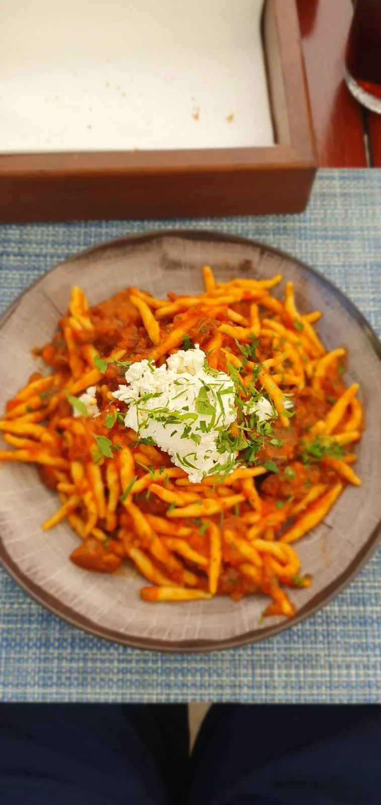 A plate of spicy orange curly fries topped with a dollop of white sauce and garnished with chopped green herbs. The plate rests on a blue placemat, alongside an empty brown tray.