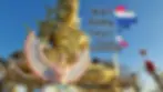 Golden statue of a deity at Wat Phra That in Doi Saket, with a bird-like figure in front. Text reads "Wat Phra That Doi Saket" alongside Thai national colors map. Clear blue sky in background.