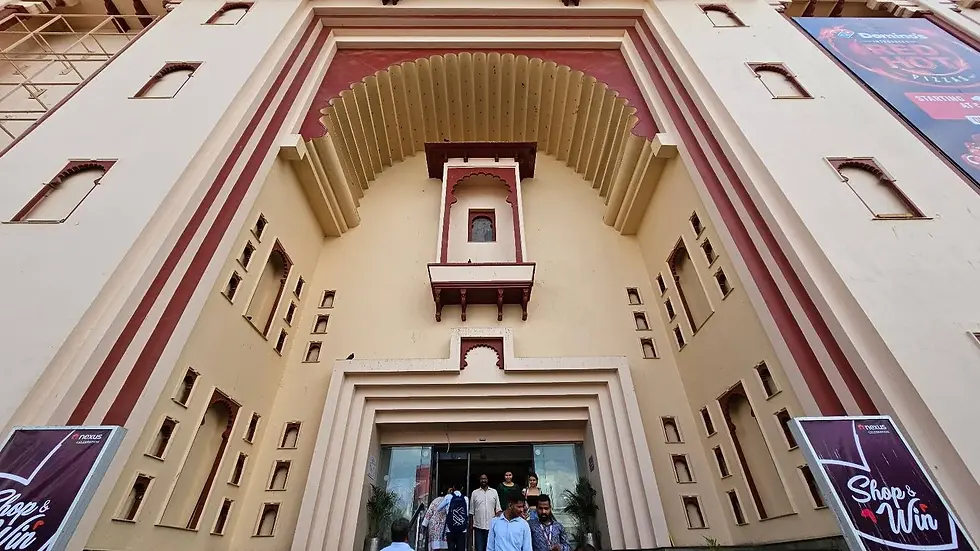 Grand entrance of a building with intricate arches and red accents. People walk out, signs read "Shop & Win." Sunny day.