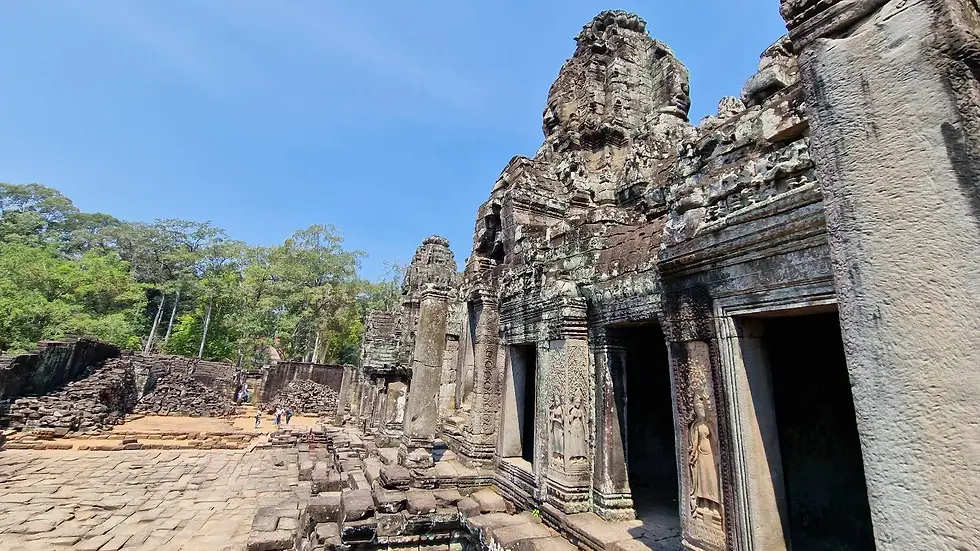 Ancient stone temple in Angkor, with intricate carvings and tall columns under a clear blue sky. Lush trees are in the background.