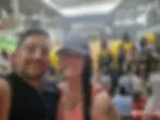 A smiling couple takes a selfie at an elephant show. Elephants with yellow and red blankets are in the background. The arena is crowded.