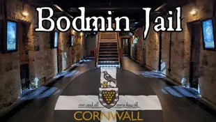 Interior view of Bodmin Jail in Cornwall, featuring a dark stone corridor with historic information posters on walls and a decorative crest on the floor.