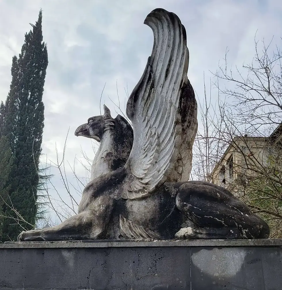 Statue of a griffin with spread wings against a cloudy sky backdrop.