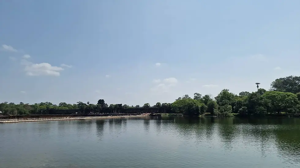A calm lake reflects lush greenery and a distant ancient stone structure under a clear blue sky.