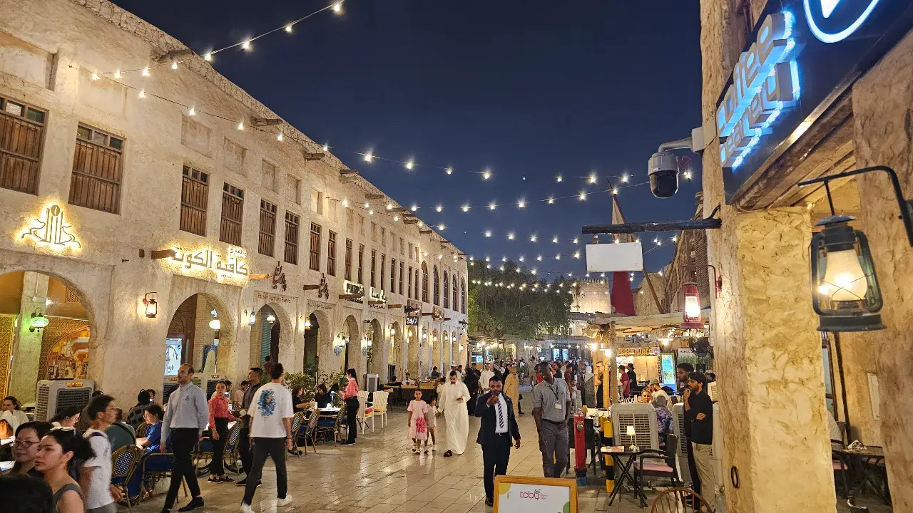 People walking along the illuminated street at Souq Waqif in Doha, Qatar, under night sky.