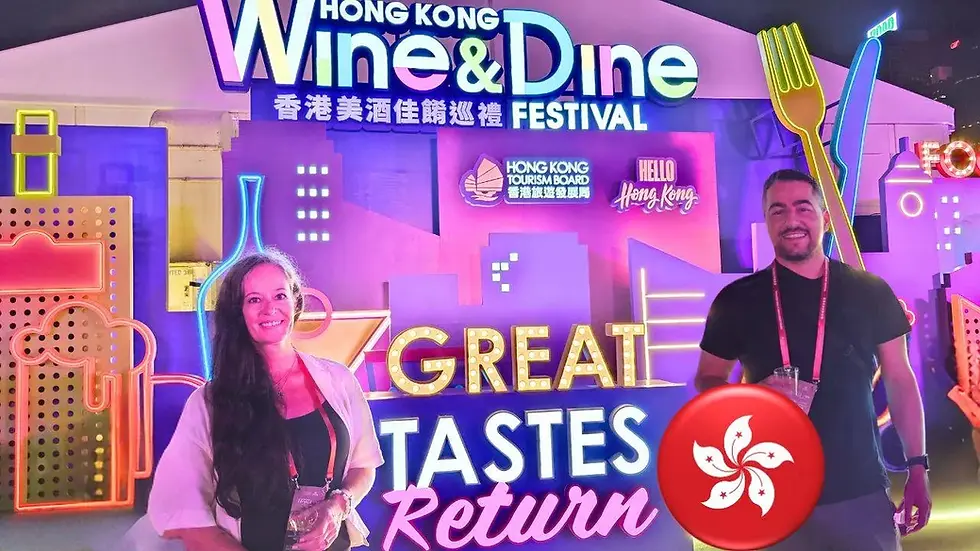 Two people stand in front of a colorful backdrop promoting the Hong Kong Wine & Dine Festival. The sign reads "Great Tastes Return" with various neon graphics and the Hong Kong Tourism Board logo.