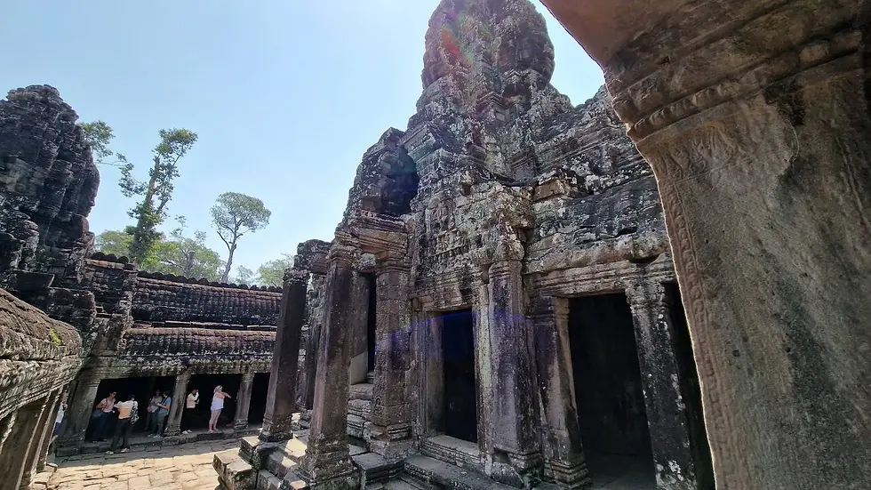 Ancient stone temple with intricate carvings under a bright blue sky. Tourists explore the ruins. Tall trees in the background.