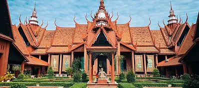The National Museum of Cambodia in Phnom Penh, featuring ornate reddish-terracotta architecture, pointed spires, and a manicured garden courtyard with a statue.