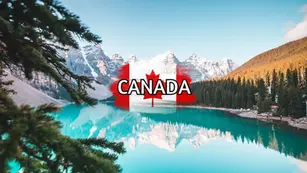 A picturesque view of a serene lake surrounded by pine forests and snow-capped mountains under a clear sky, capturing one of Canada's must-visit spots. A semi-transparent Canadian flag with the word "CANADA" is superimposed over the scene.