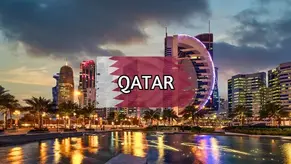 Skyline of Doha at sunset featuring illuminated skyscrapers and the Qatar flag with bold text overlay reading QATAR.