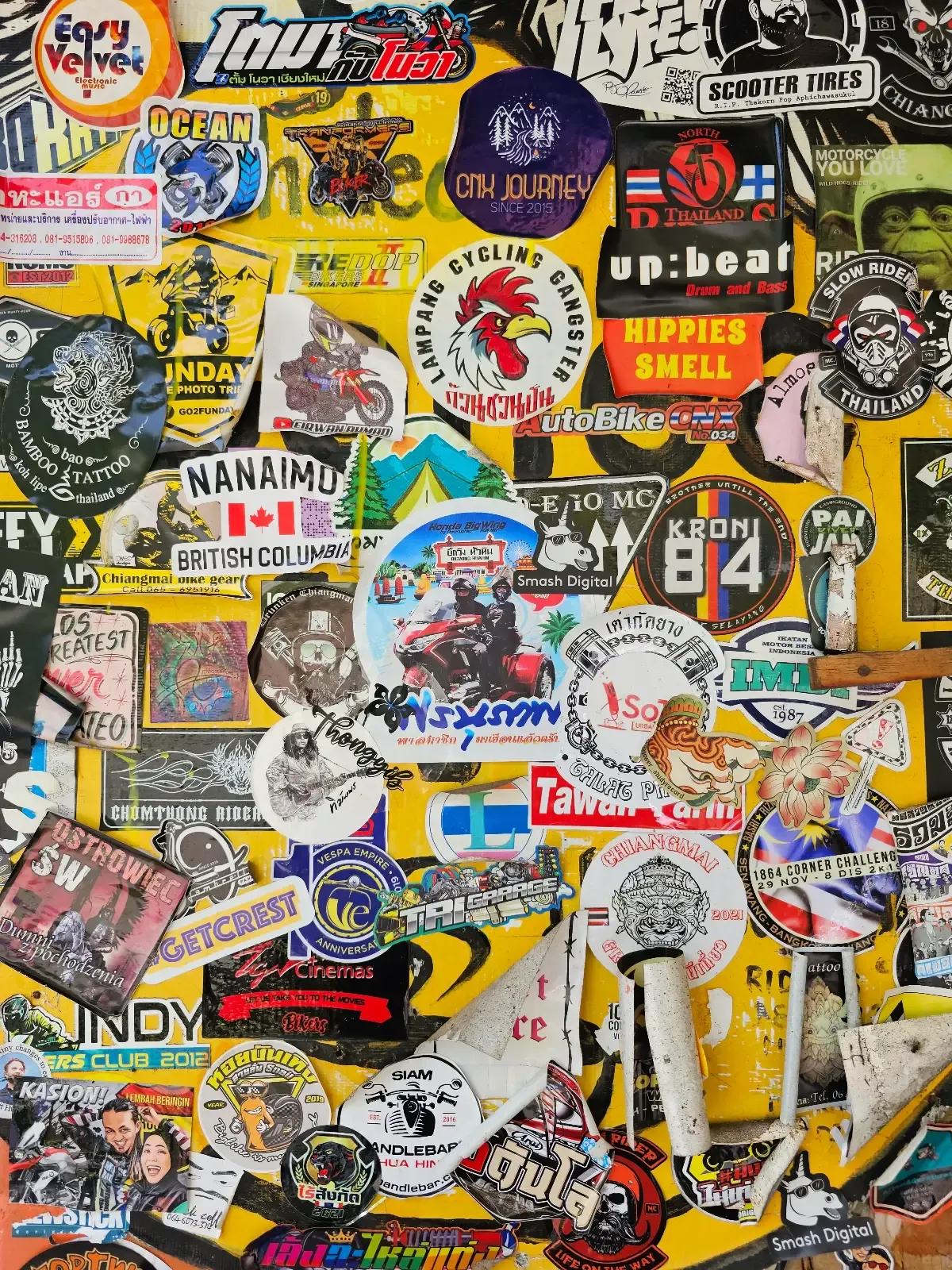 A colorful collage of various stickers is displayed on a yellow background. The stickers feature logos, text, band names, cartoon characters, and graphics in different shapes and sizes, overlapping each other densely.