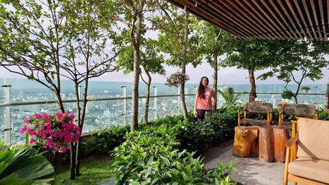A woman standing in the rooftop garden at SALA Danang Beach Hotel, with city views and landscaped greenery.