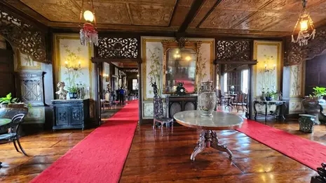 Interior of Casa Manila Museum with antique furniture, wooden floors, decorative screens, and red carpet runners.