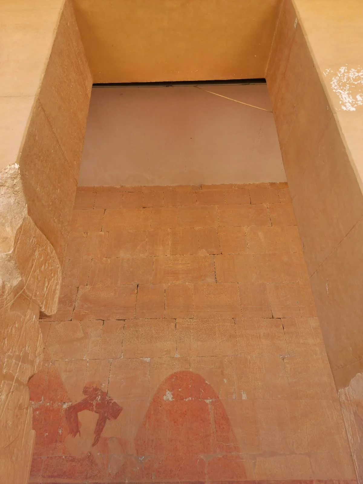 Interior view of a tall, narrow structure with a large rectangular wall. The walls and floors are in shades of earthy brown, with some signs of wear. There are faint markings or patterns near the base. The ceiling is not visible.