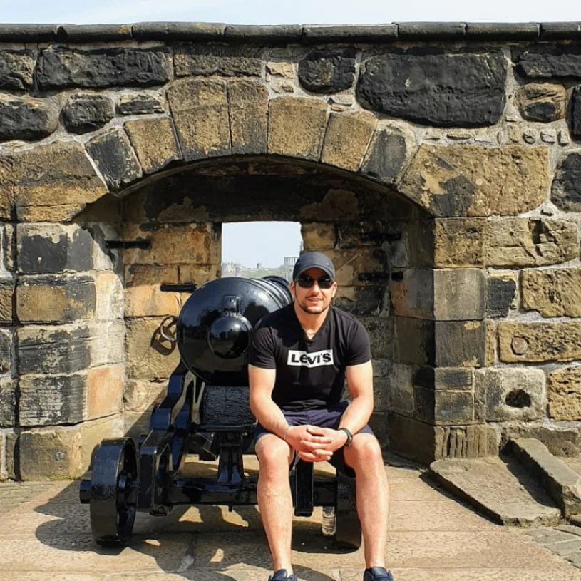Leon sitting beside historic cannons against a stone wall at Edinburgh Castle.