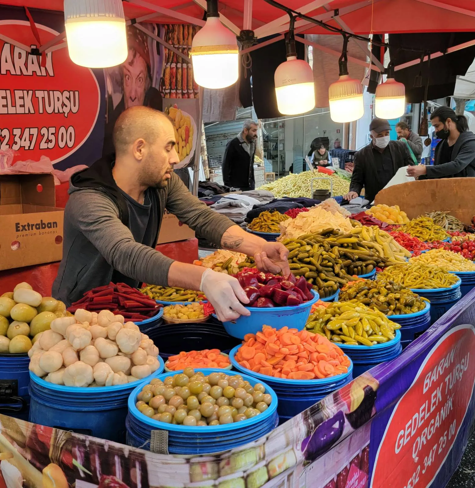 Man arranging bowls of pickled vegetables at an outdoor market stall.