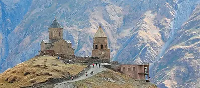 The historic Gergeti Trinity Church situated on a steep hill against the backdrop of the massive, rugged Caucasus Mountains.