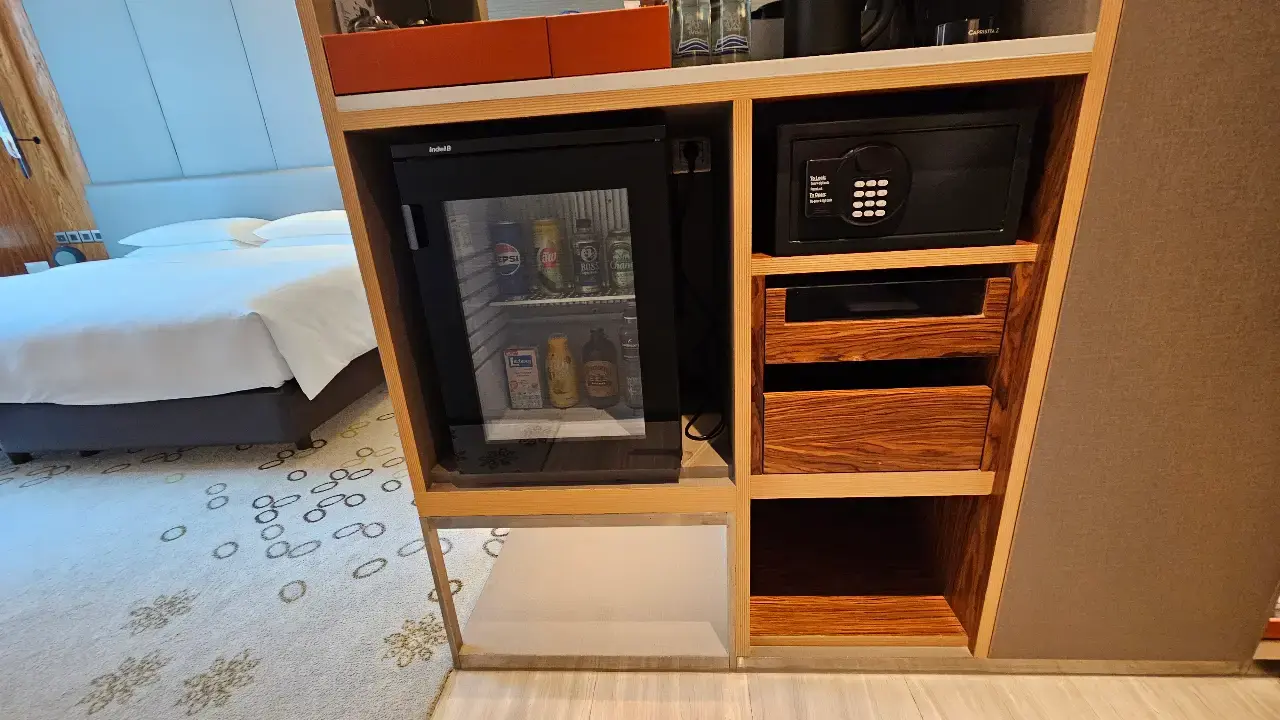 Minibar cabinet with a mini fridge, storage shelves and in-room safe.