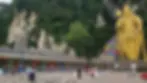 Huge golden statue, colorful temple, and rainbow stairs in lush, green setting. People gather, pigeons scatter. Serene atmosphere.