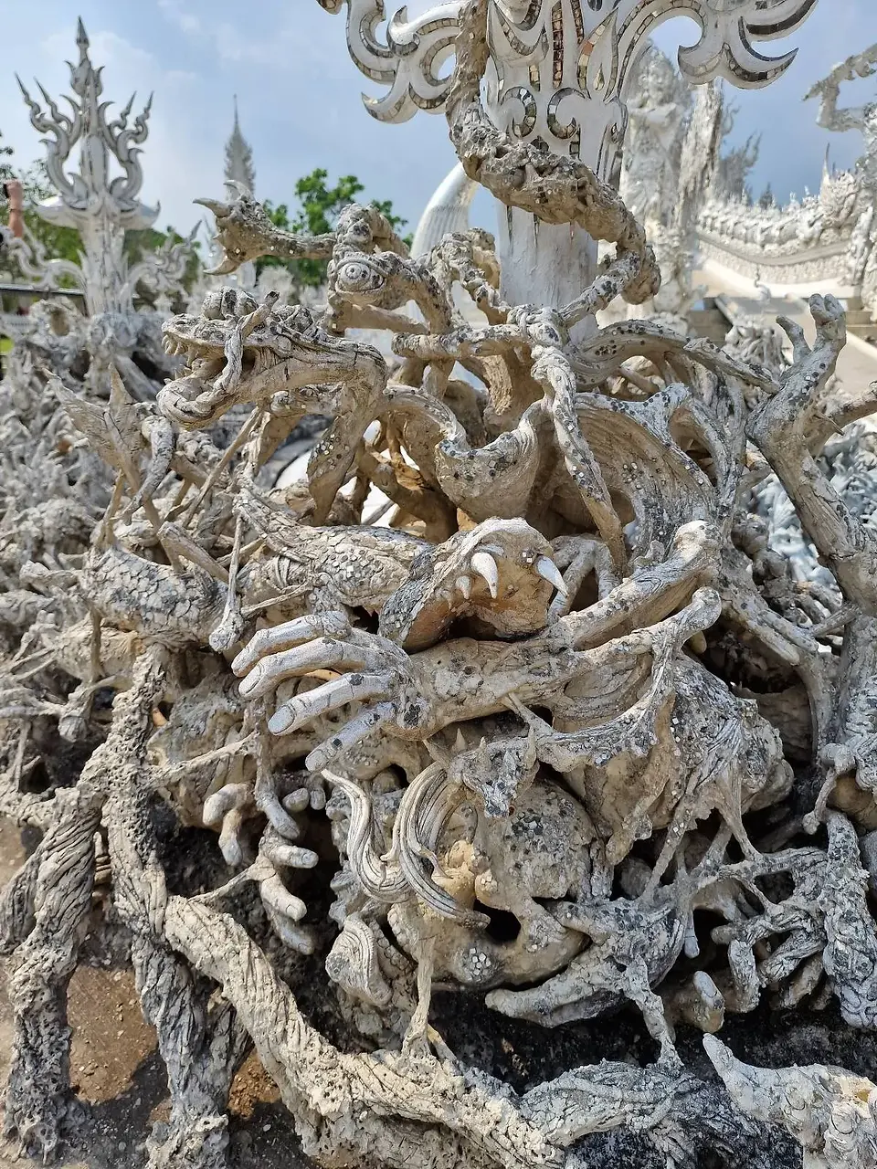 Elaborate white sculptures featuring intricate and twisted designs inspired by organic shapes, such as roots and branches, set against a bright sky.