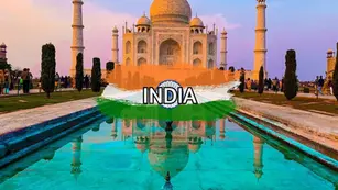 The Taj Mahal at sunset with its reflection in a long pool, surrounded by gardens and visitors. The word "INDIA" and an Indian flag overlay are at the bottom of the image.