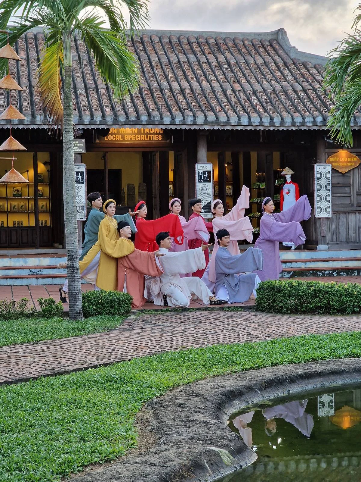 Group of people in traditional Vietnamese attire posing in front of an old-style building with a tropical landscape.