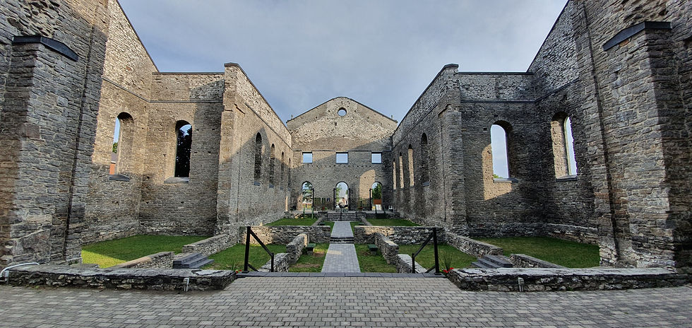 Ruined stone building with arched windows, green grass, and cobblestone paths. Bright sky backdrop, creating a serene, historical mood.
