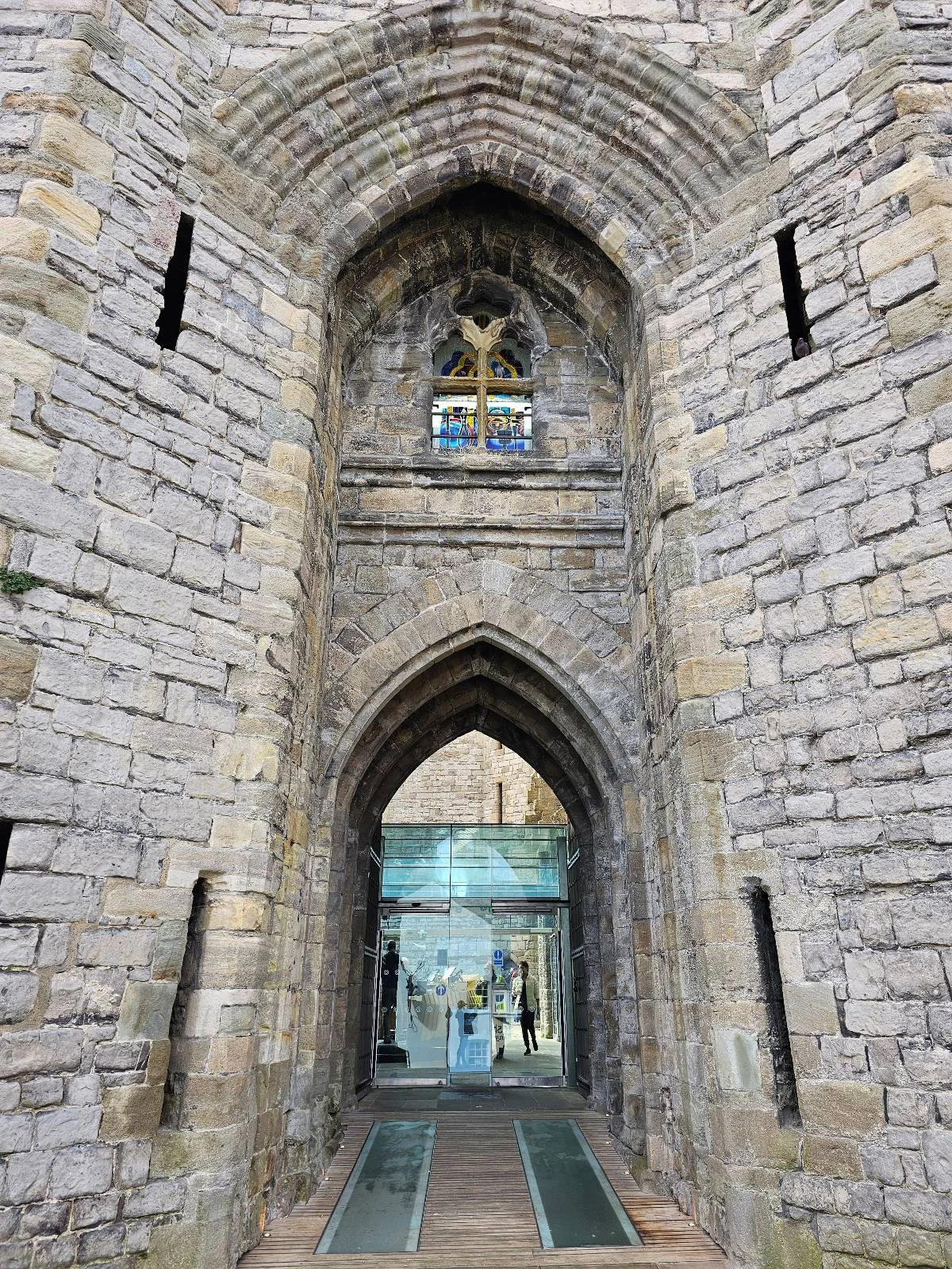 Stone archway entrance of a historic building with thick walls, narrow windows, and a glass door visible through the arch.