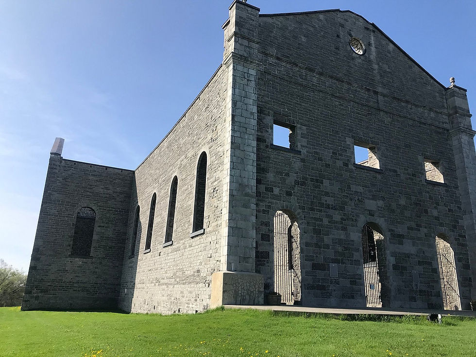 Old stone building ruins with arched windows, set against a clear blue sky. Green grass surrounds the structure, creating a serene mood.