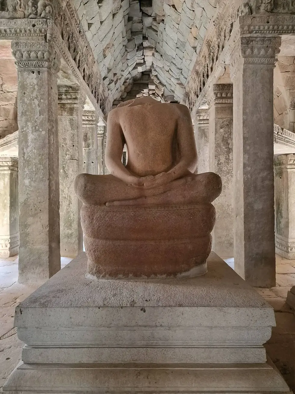 Stone Buddha statue with missing head, seated cross-legged in ancient temple corridor, surrounded by detailed stone pillars and muted tones.
