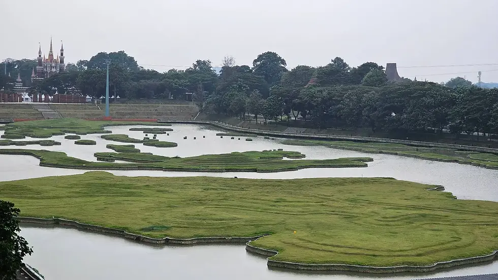 Green islands in a water feature surrounded by trees. A castle is visible in the distance under an overcast sky, creating a serene mood.