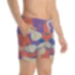 A person is wearing colorful shorts with a bold, abstract pattern in purple, red, and gray, standing with hands on hips.