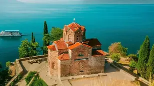 Church of St. John at Kaneo perched on a cliff above Lake Ohrid, with terracotta roof tiles, stone walls, and deep blue water below, North Macedonia.