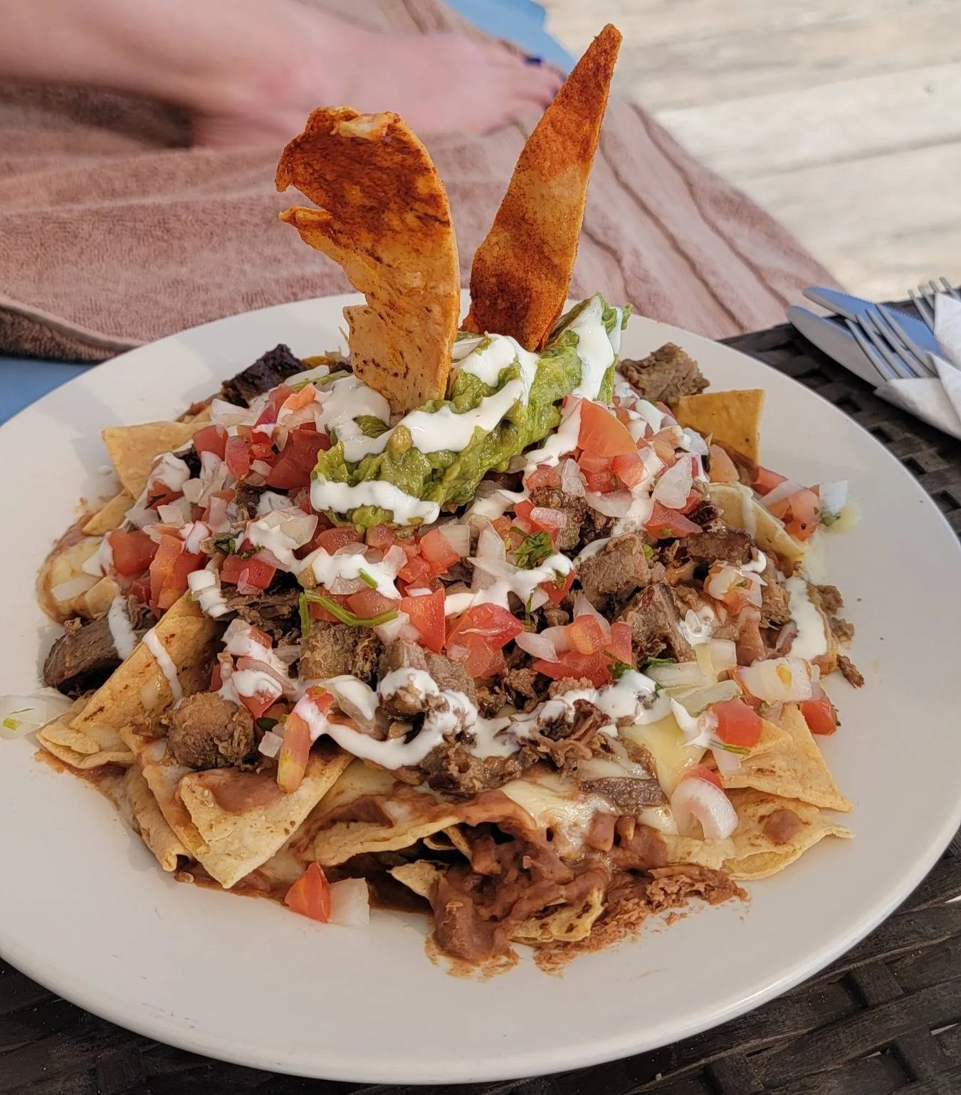 A plate of nachos with melted cheese, diced tomatoes, beef, and a drizzle of sour cream, topped with guacamole and two tortilla chips standing upright.