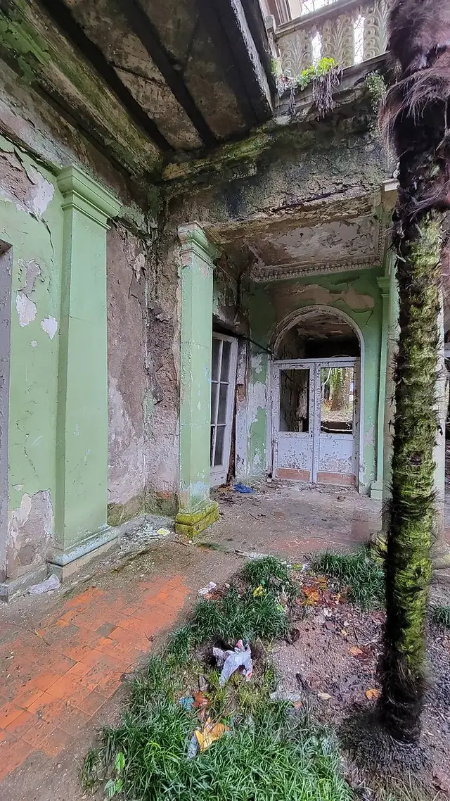 Dilapidated interior of an abandoned building with peeling paint and overgrowth.