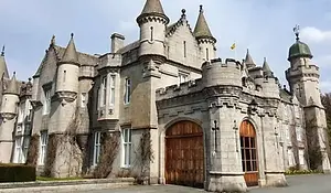 Balmoral Castle in Aberdeenshire, featuring granite towers, turrets, and arched wooden doors set within the Balmoral Estate.