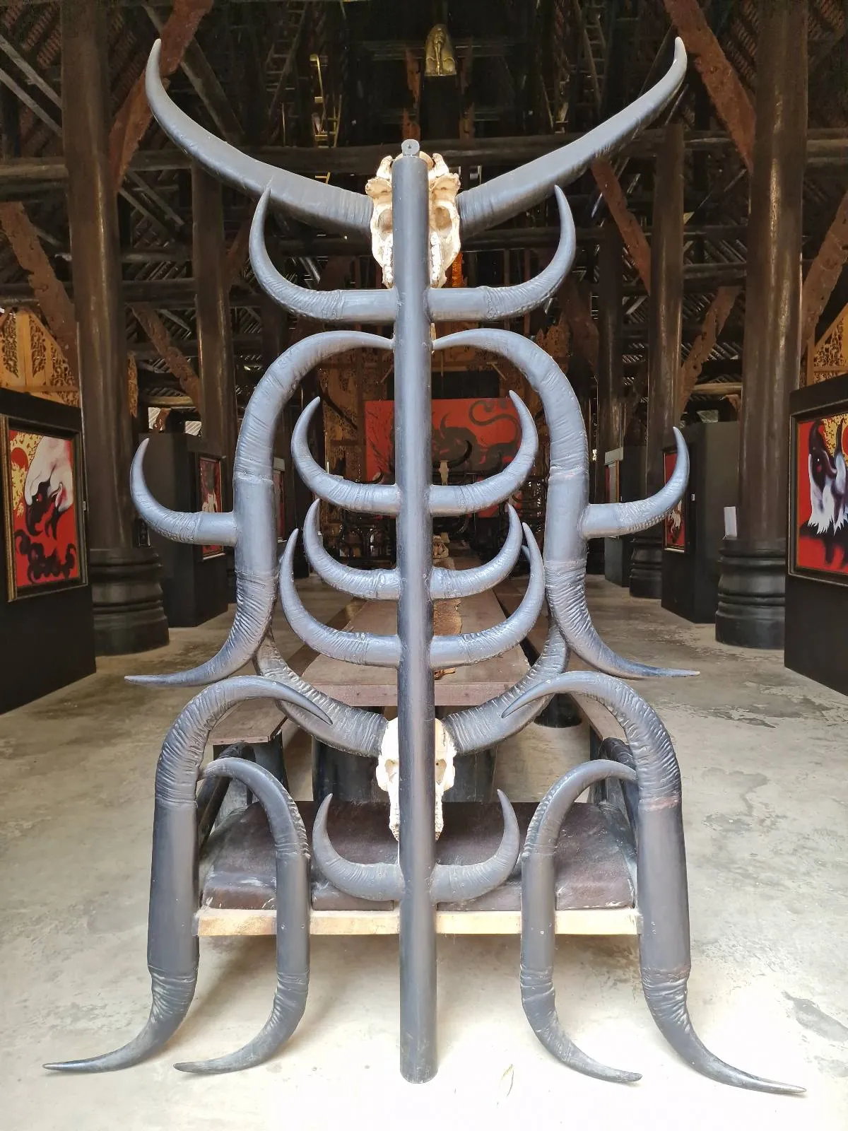 An intricately designed wooden chair with numerous large curved horns, positioned in a dimly lit room with wooden beams.