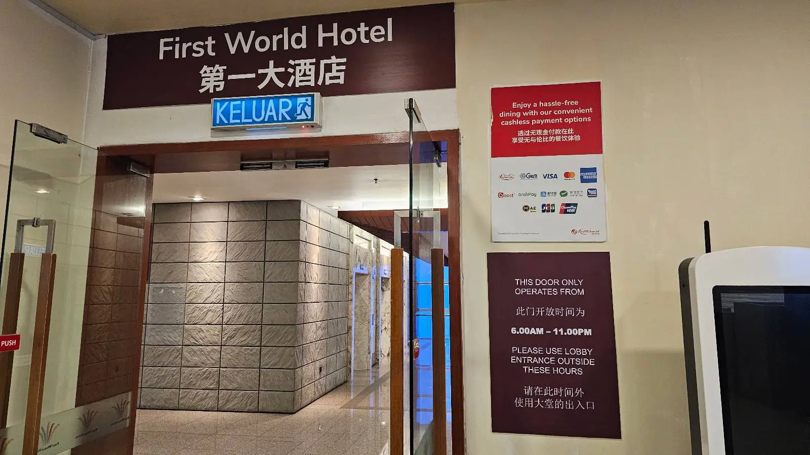 Entrance to First World Hotel with signs in English and Chinese, a glass door, and various informational displays including accepted payment methods on the right wall.