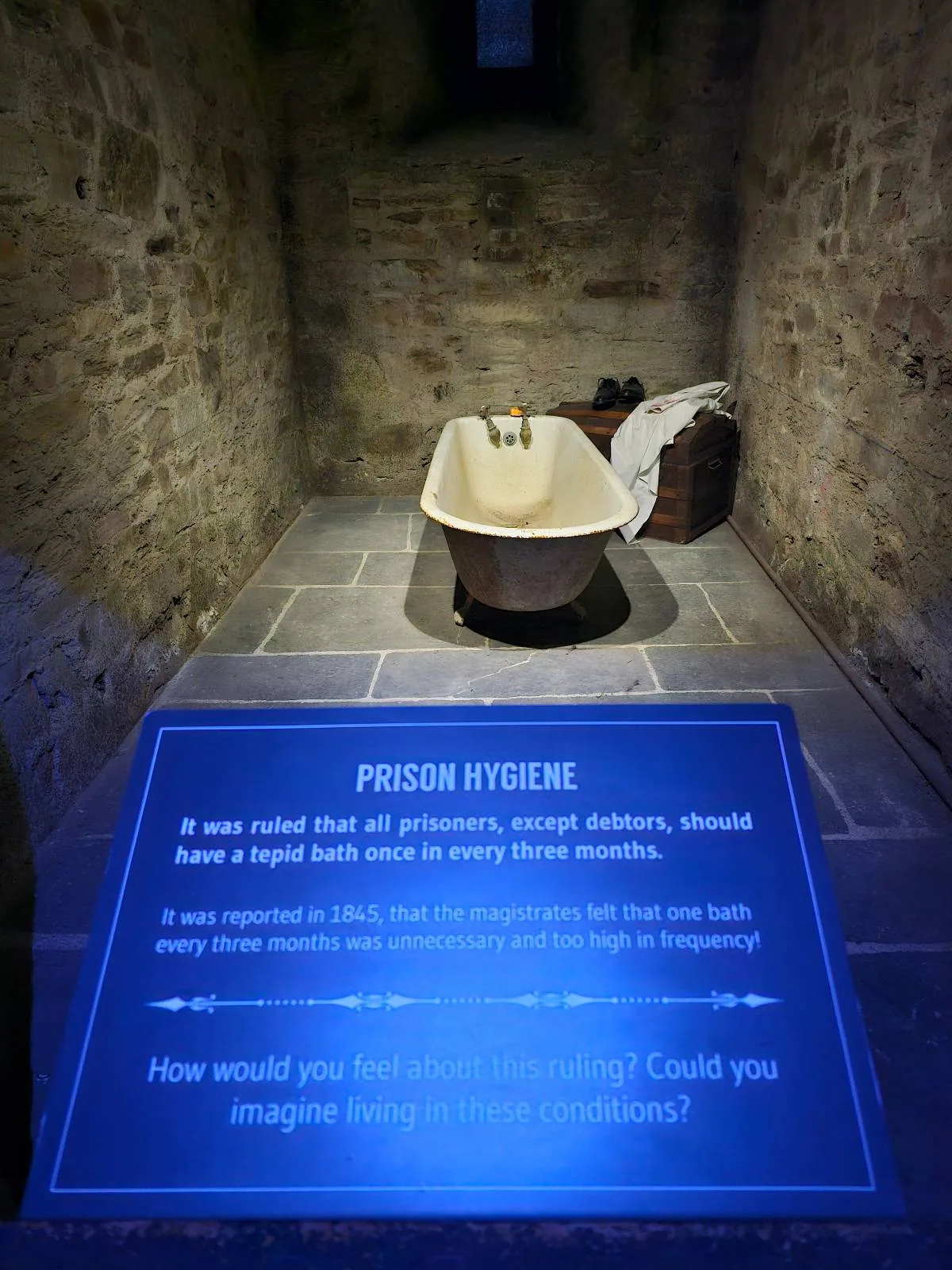 An old bath in small stone dimly-lit room with an informational plaque about a "prison hygiene".