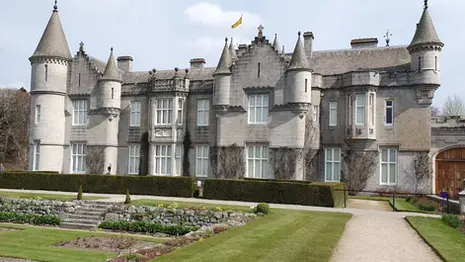 Exterior view of Balmoral Castle with stone towers, landscaped gardens, and surrounding woodland.