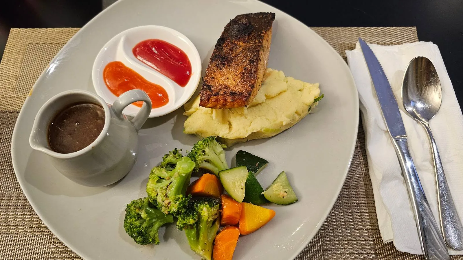 A modern restaurant interior with green cushioned chairs and tables set for dining. Large windows line the right side, letting in natural light. A few people are seated, and wooden light fixtures hang from the ceiling.