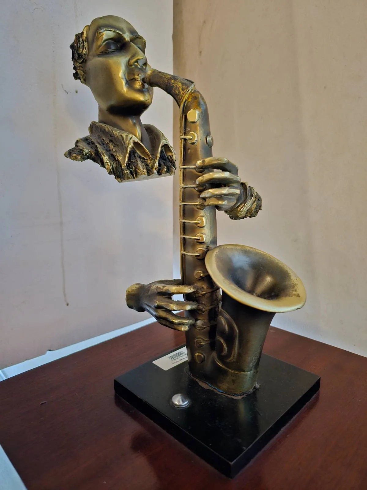A bronze sculpture of a saxophonist featuring a head, hands, and saxophone emerging from a base. The musician's lips are poised as if blowing into the instrument, creating a dynamic and artistic impression against a neutral backdrop.