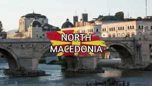 A historic stone bridge spans a river with elegant, classic buildings in the background. "North Macedonia" is prominently displayed over a red and yellow design in the center.