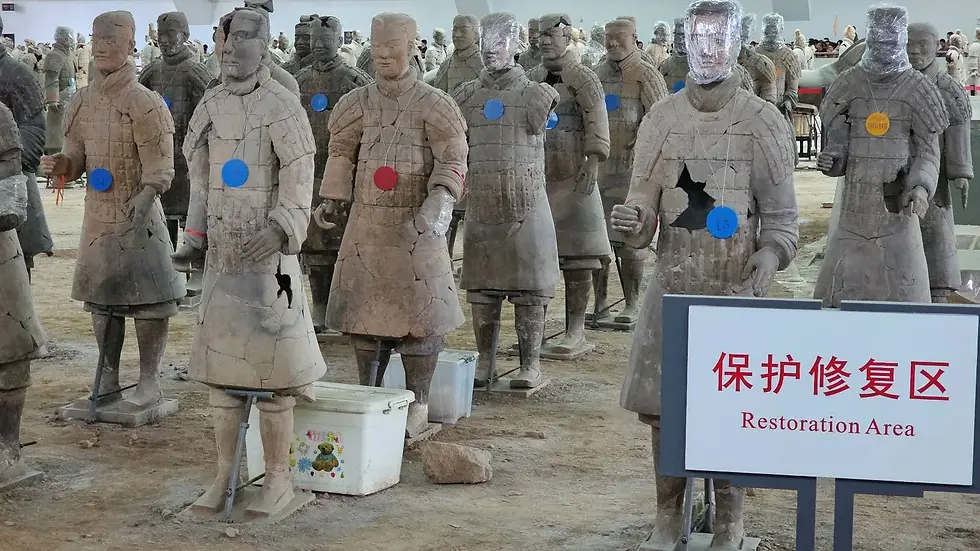 Terracotta soldiers in various stages of restoration, many with blue or red tags, stand on dirt. A sign reads "Restoration Area."