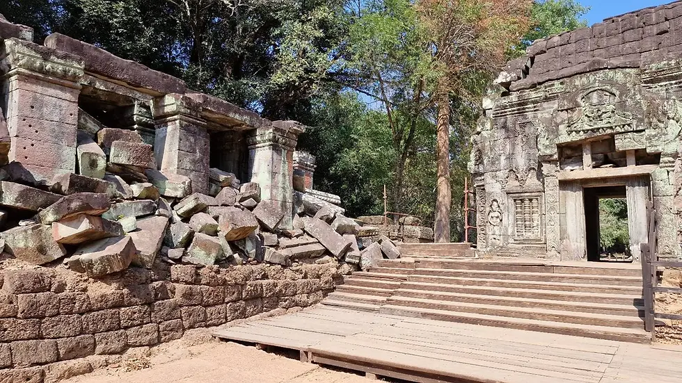 Ancient stone temple ruins with a crumbling facade and intricate carvings. Surrounded by lush green trees and a wooden pathway. Calm atmosphere.