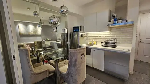 Modern kitchen and dining area with glass table, tufted chairs, mirrored backsplash, and pendant lights. Bright, clean, and stylish decor.
